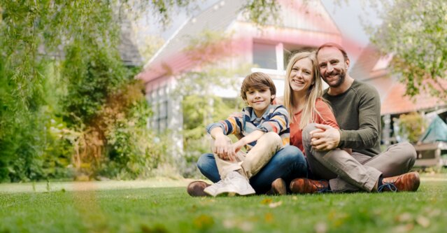 Eine glückliche Familie entspannt vor ihrem Eigenheim – Zuverlässige Energieversorgung mit Ökostrom, Erdgas und Heizöl von MONTANA